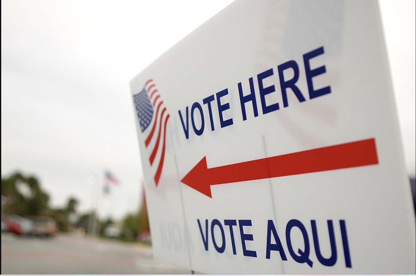 Voting sign directing individuals to the polling location with bilingual instructions in English and Spanish, featuring an American flag design.