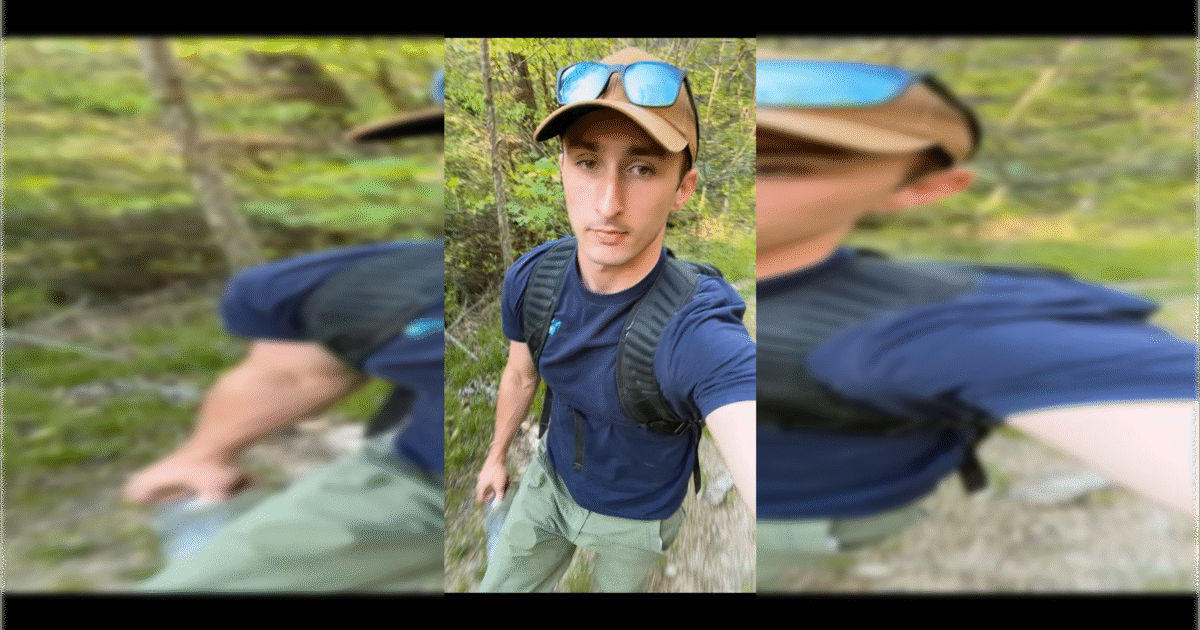 Young man hiking on a forest trail, wearing a cap and sunglasses, holding a water bottle, surrounded by greenery.