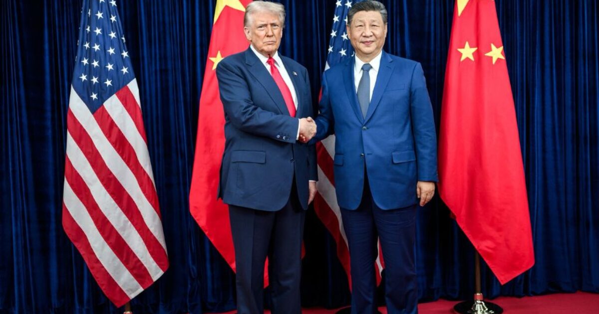 Donald Trump and Xi Jinping shake hands during a diplomatic meeting, flanked by the flags of the United States and China.