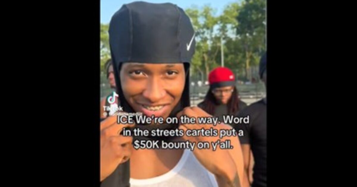 Young man smiling in a park setting, wearing a black cap, with a group of friends in the background, referencing a $50K bounty in a TikTok video.