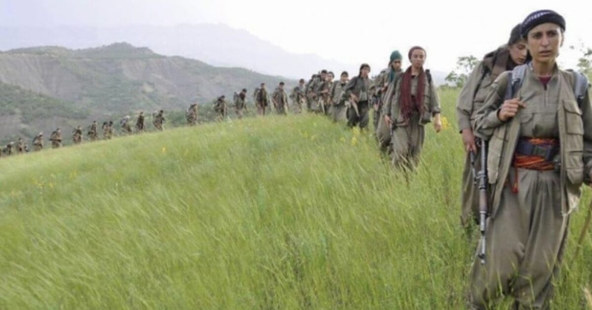 Kurdish fighters march through a grassy landscape, showcasing their commitment and readiness in a mountainous region.