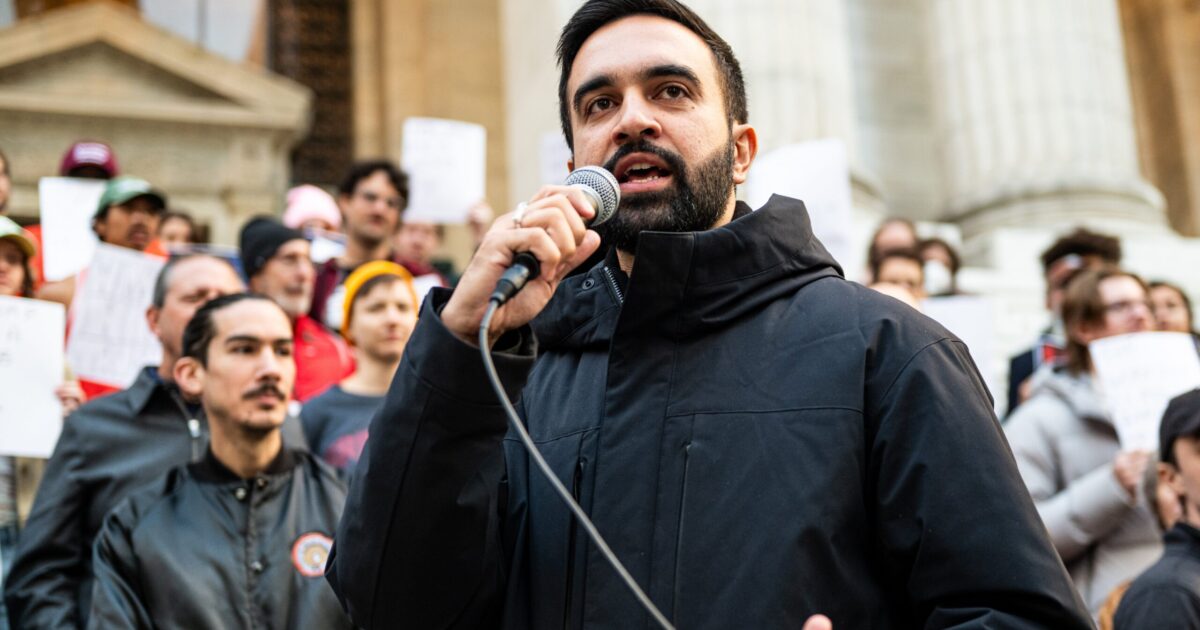 A speaker addresses a crowd during a protest, holding a microphone and advocating for social change outside a historic building.