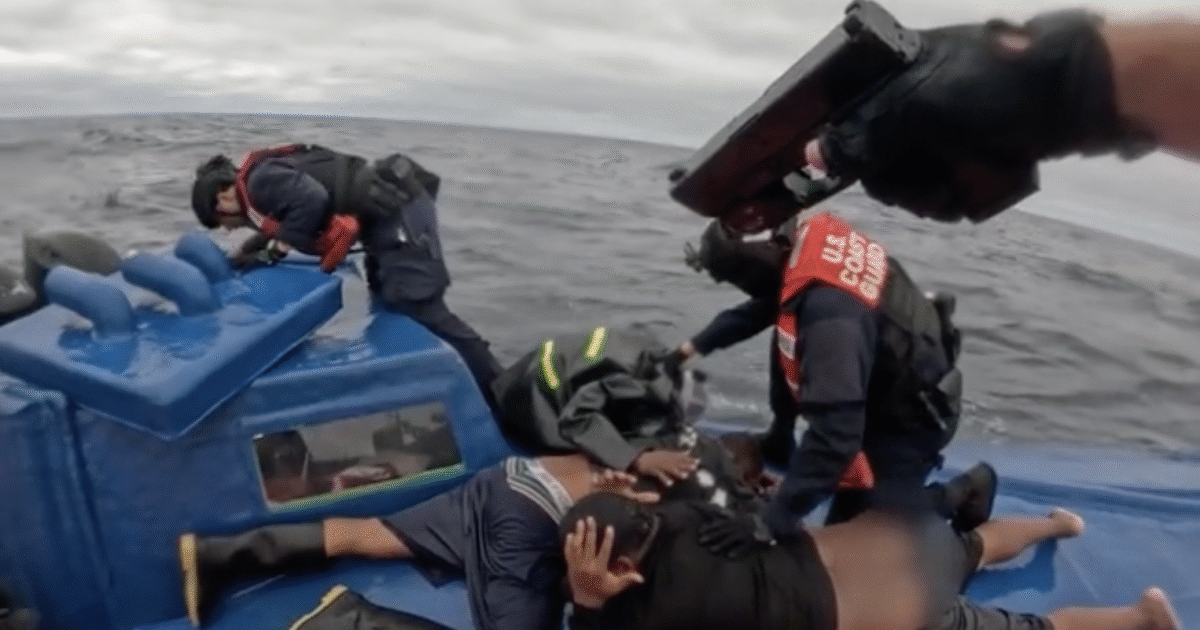 U.S. Coast Guard personnel apprehend individuals on a blue boat at sea during a law enforcement operation.