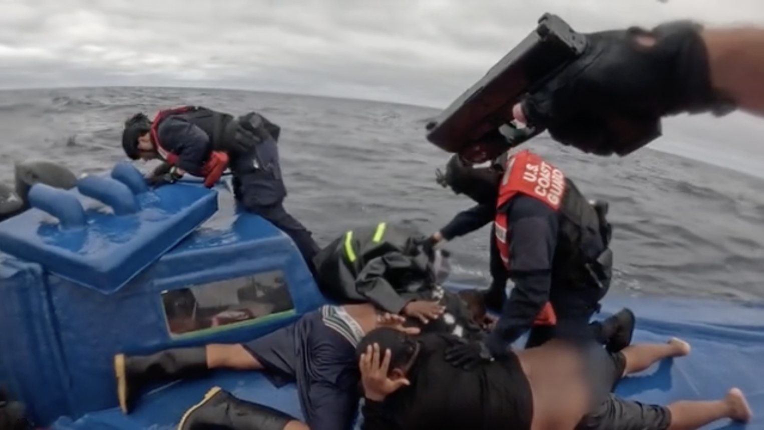 U.S. Coast Guard personnel apprehend individuals on a blue boat at sea during a law enforcement operation.