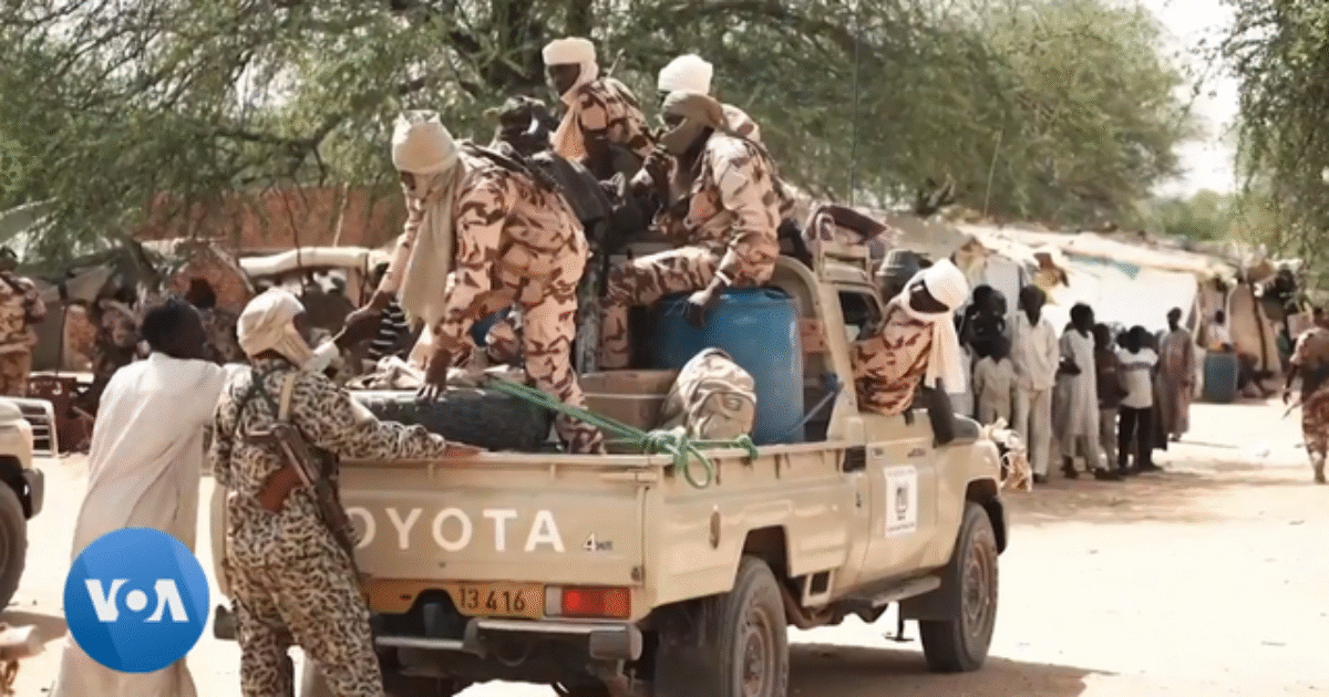 Soldiers in camouflage uniforms load supplies onto a Toyota pickup truck in a desert setting, with people and tents visible in the background.