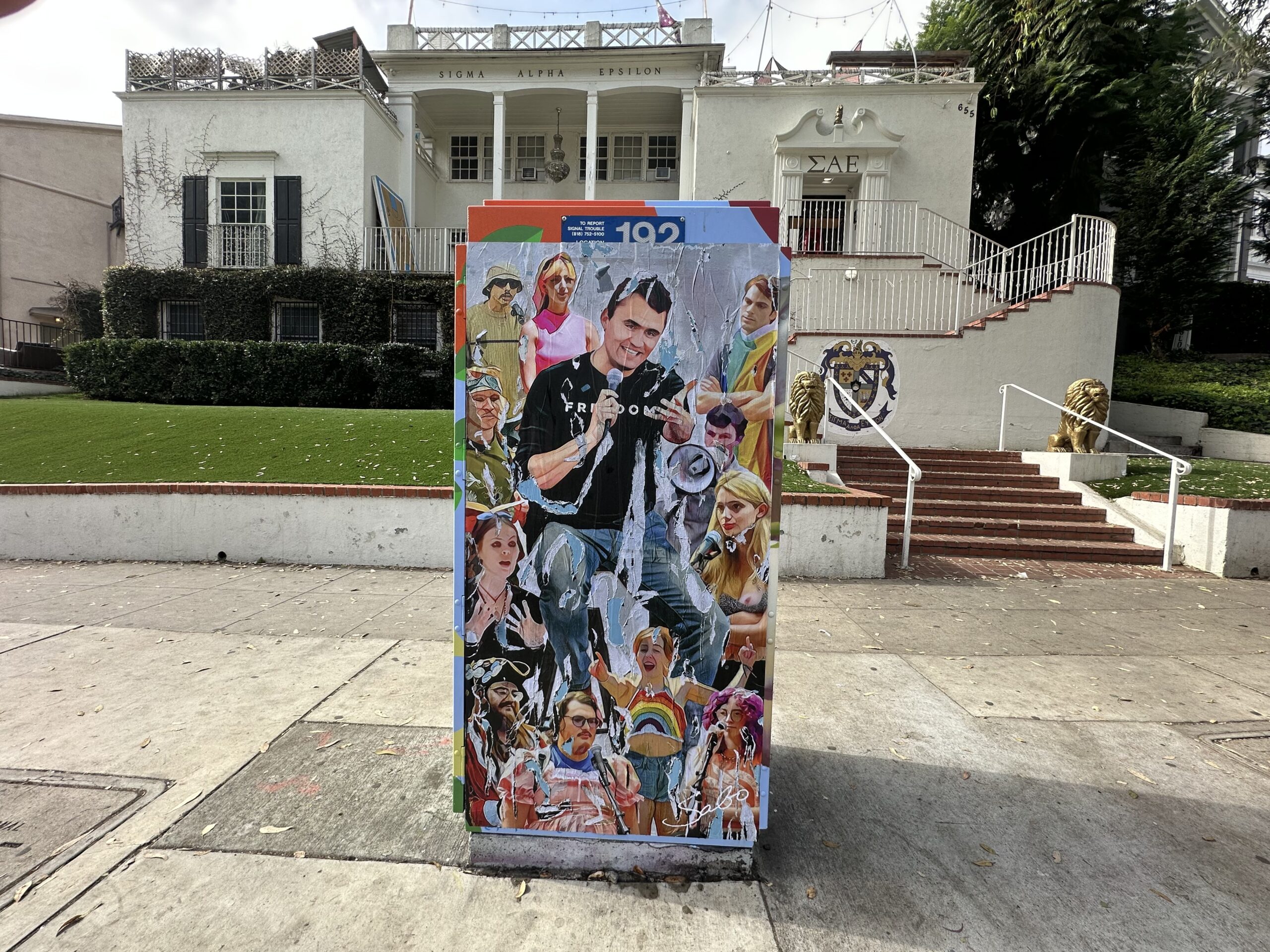 Colorful street art mural featuring various characters on a utility box in front of a historic building, showcasing vibrant urban culture.