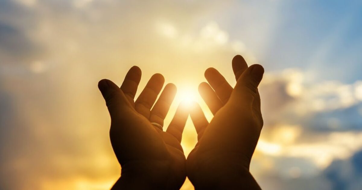Hands reaching towards a bright sun against a cloudy sky, symbolizing hope and connection with nature.