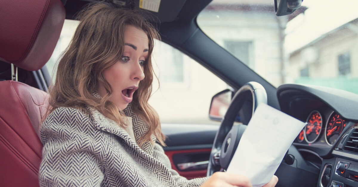 Surprised woman in a car looking at a document, conveying shock or disbelief in a modern vehicle interior.