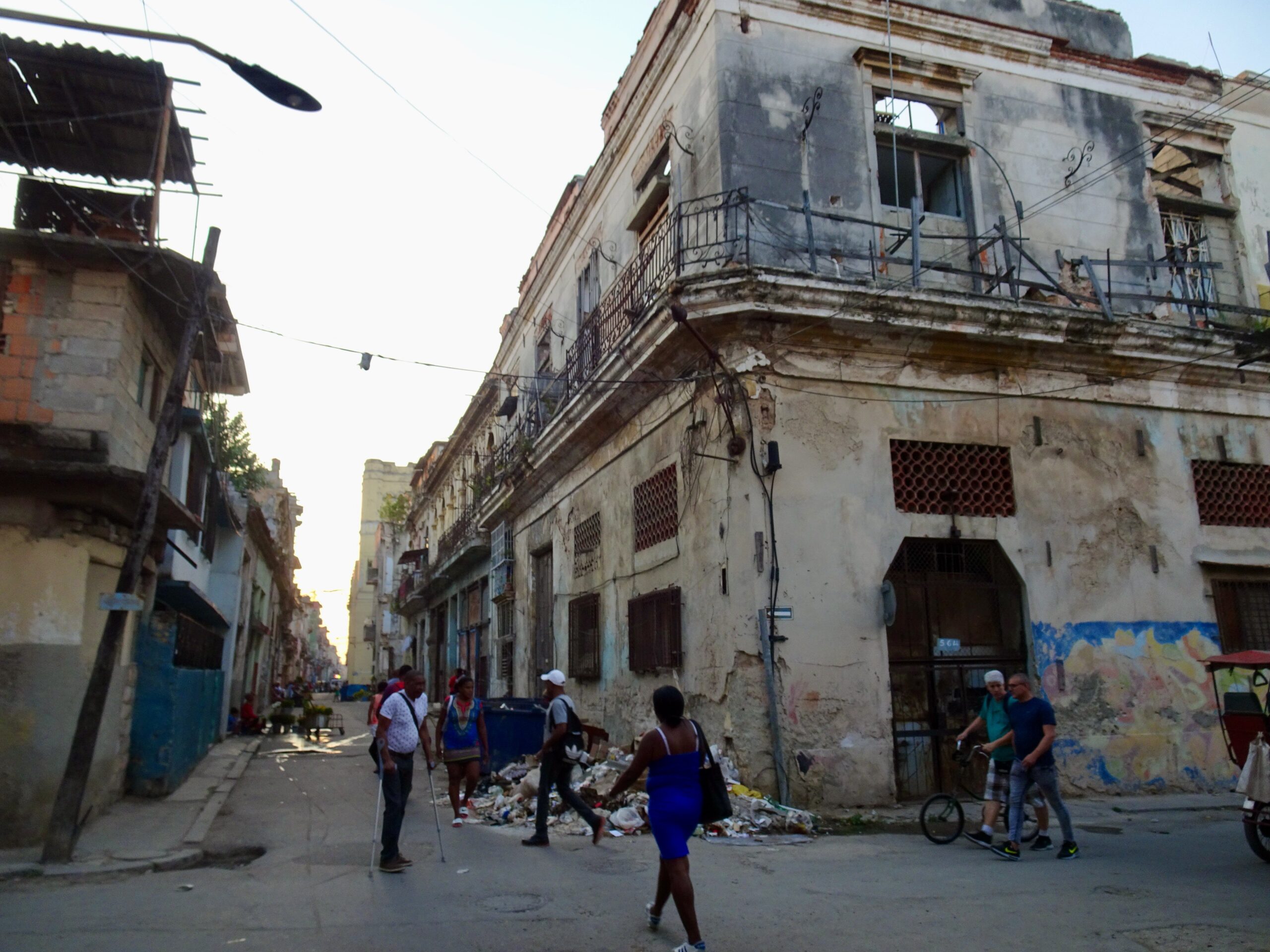 Busy street scene in Havana featuring dilapidated buildings, pedestrians, and scattered debris, capturing the vibrant yet challenging urban environment.