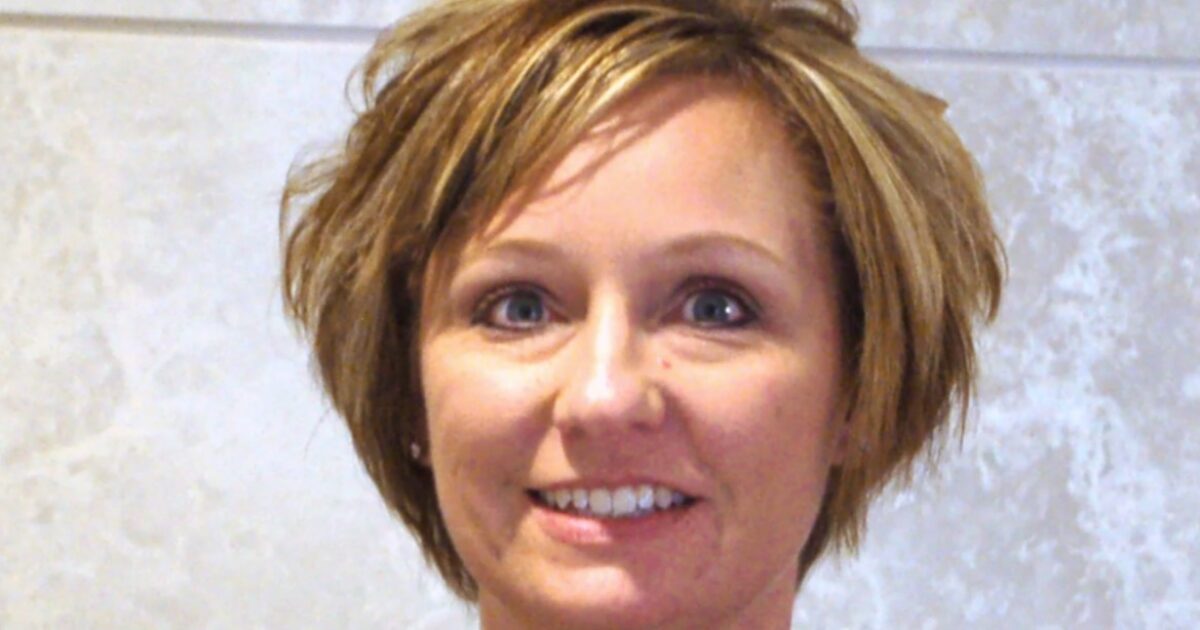 Smiling woman with short, layered hair and blue eyes against a light textured background, showcasing a friendly and approachable demeanor.