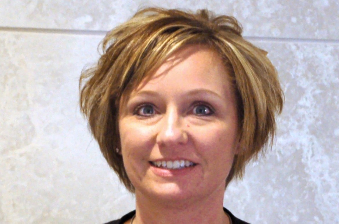 Smiling woman with short, layered hair and blue eyes against a light textured background, showcasing a friendly and approachable demeanor.