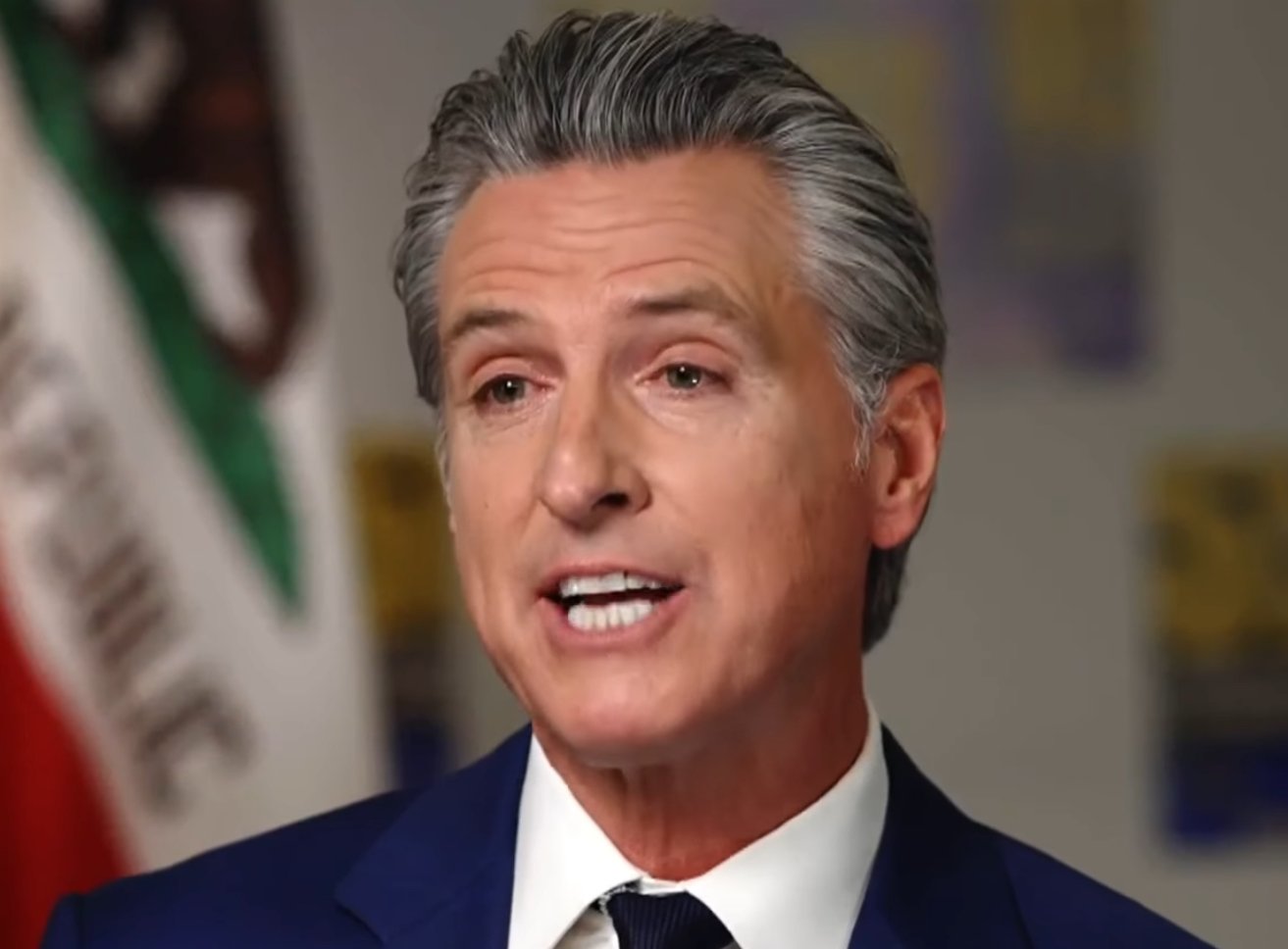 California Governor speaking during an interview, showcasing leadership and engagement in state issues with a backdrop of the California flag.
