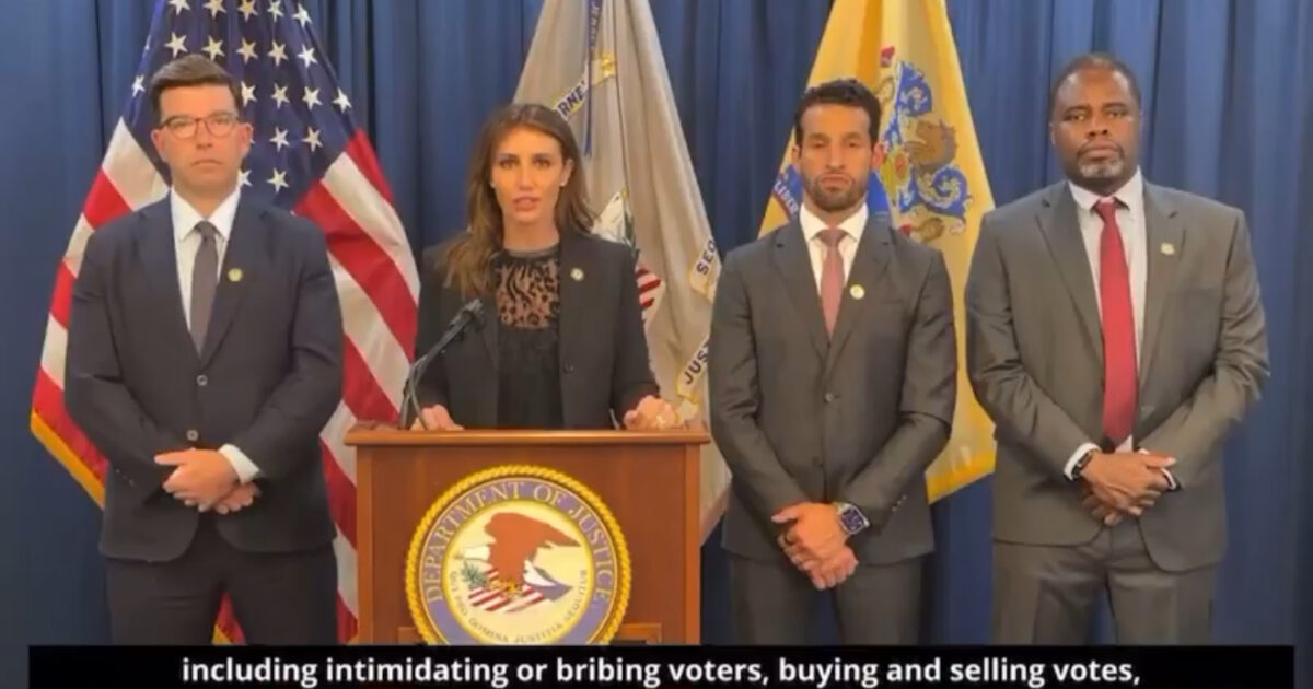 Officials from the Department of Justice address voter intimidation and election integrity issues during a press conference, standing in front of American flags.