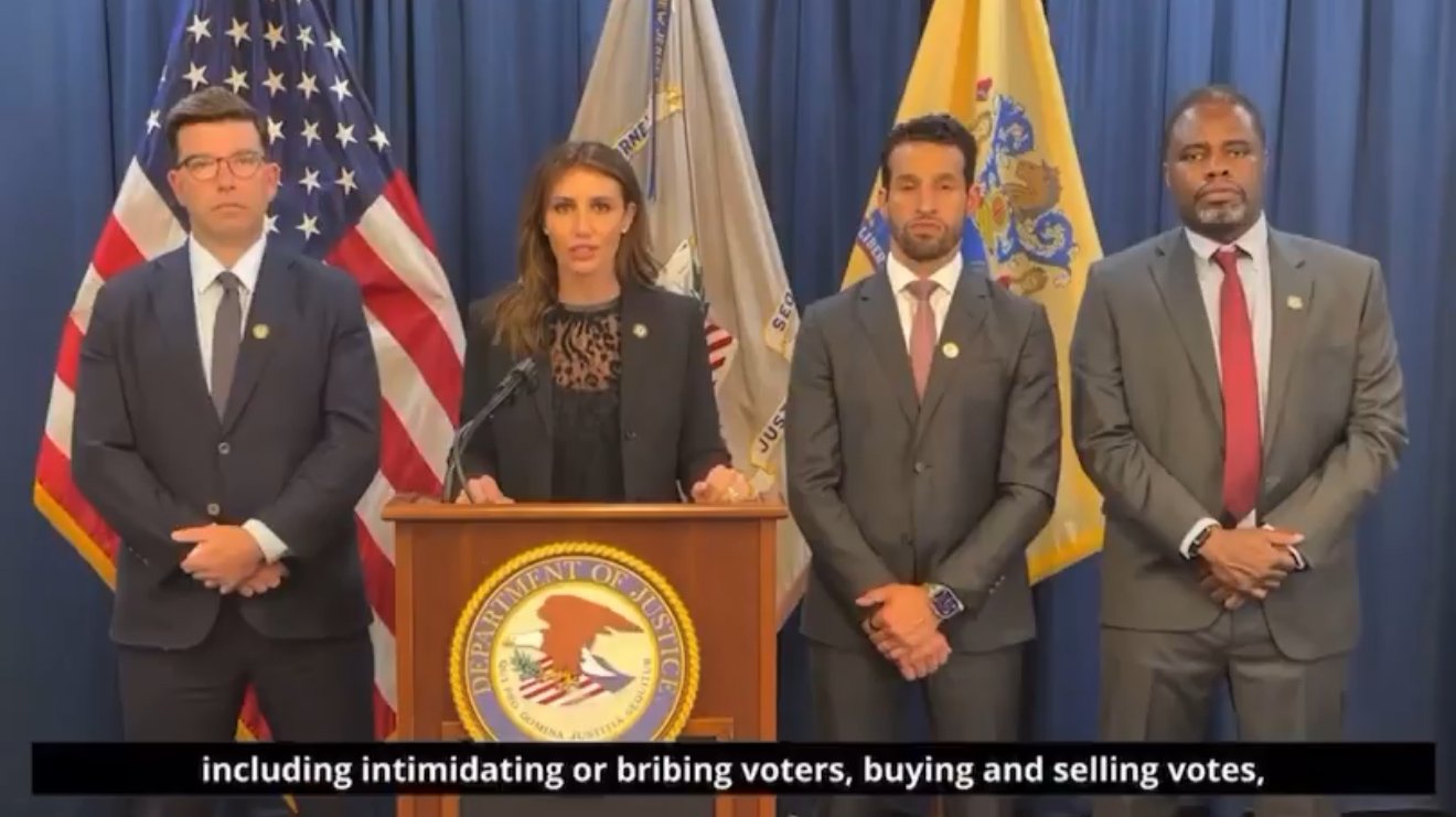 Officials from the Department of Justice address voter intimidation and election integrity issues during a press conference, standing in front of American flags.