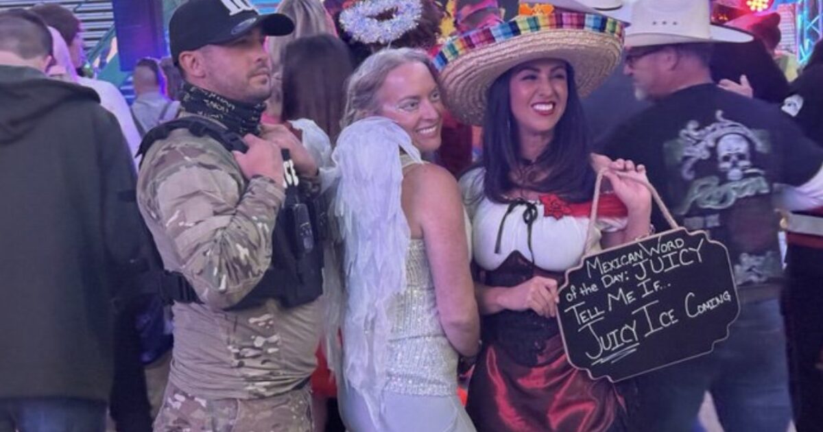 Three friends in festive costumes pose together at a lively event, featuring a soldier, an angel, and a woman in traditional Mexican attire holding a humorous sign.