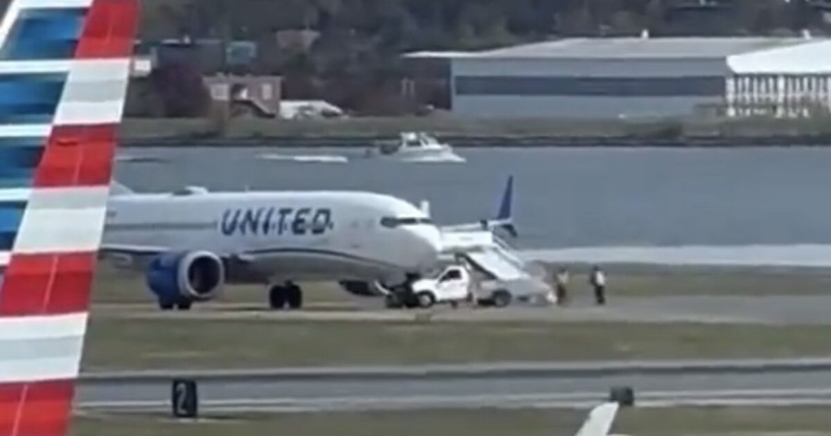 United Airlines plane on the tarmac with ground crew and service vehicle, showcasing airport operations near the water.