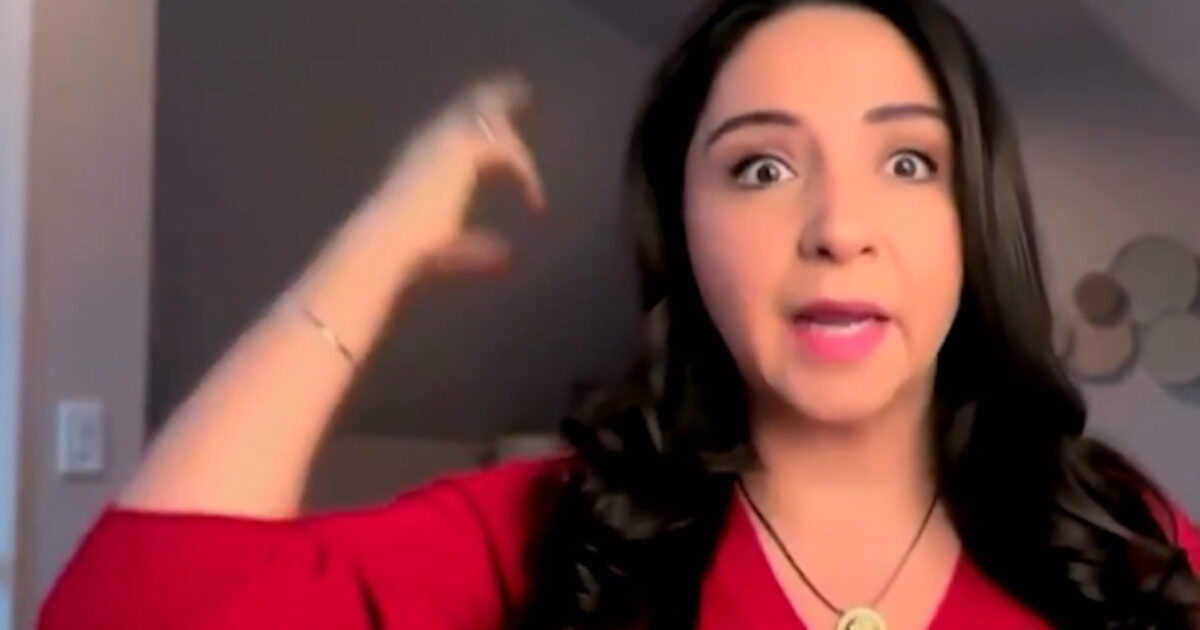 A woman in a red shirt expresses excitement or emphasis while gesturing with her hand, set against a neutral background.