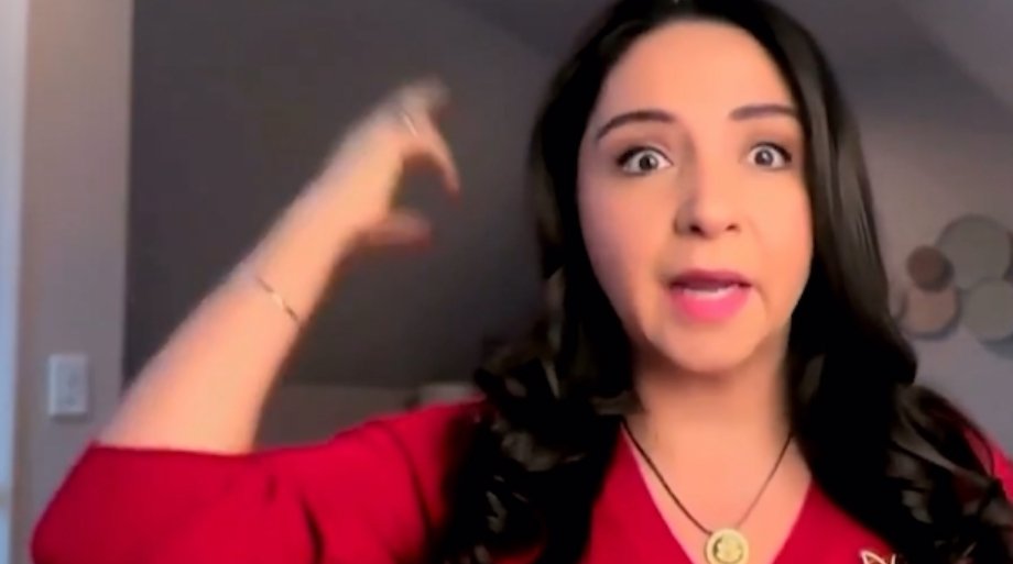 A woman in a red shirt expresses excitement or emphasis while gesturing with her hand, set against a neutral background.