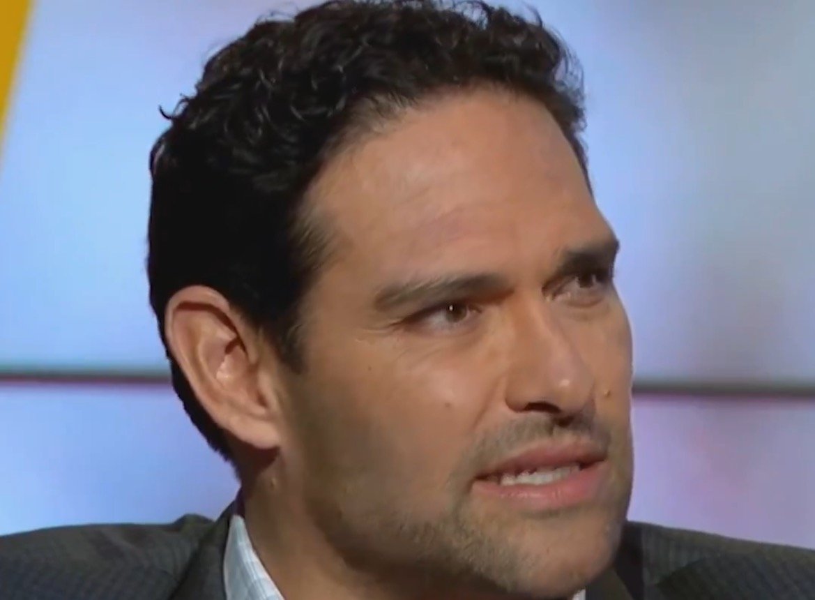 Close-up of a man with dark curly hair and a serious expression, discussing sports analysis on a television program.