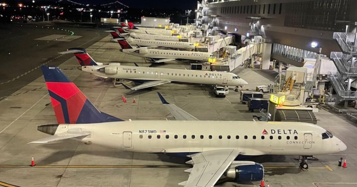 Delta Connection aircraft parked at night at an airport gate, showcasing multiple planes and terminal facilities illuminated against the dark sky.