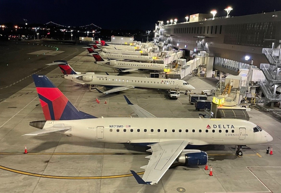 Delta Connection aircraft parked at night at an airport gate, showcasing multiple planes and terminal facilities illuminated against the dark sky.