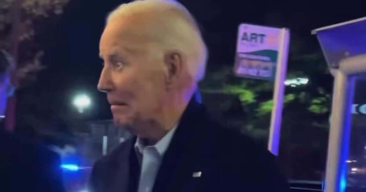 Joe Biden appears surprised while interacting with people at night, with police lights visible in the background and an ART sign nearby.