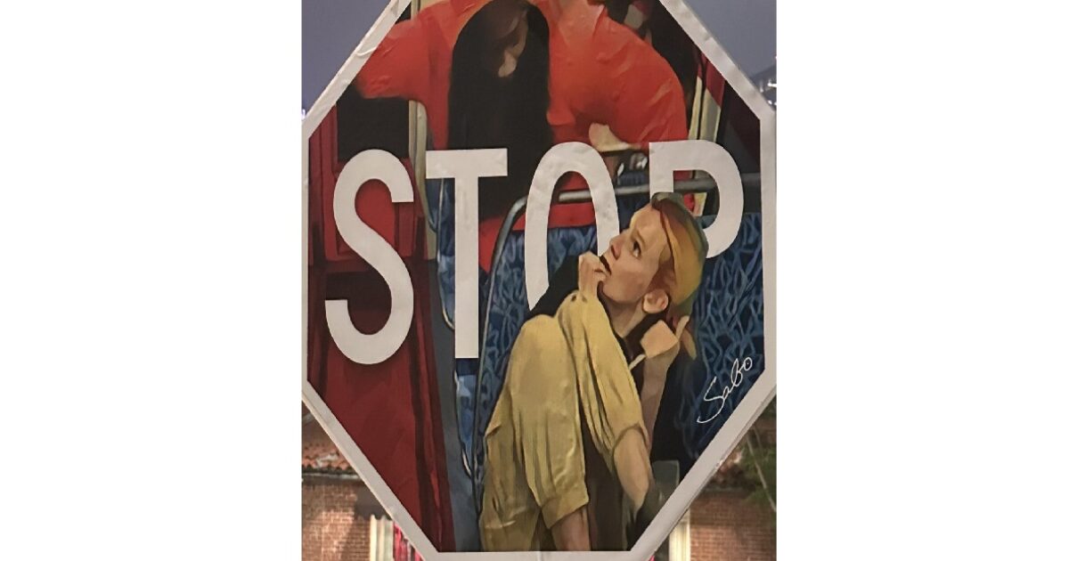 Street art featuring a painted stop sign with two figures, one in a red hood and the other with blonde hair, conveying a sense of urban life and creativity.