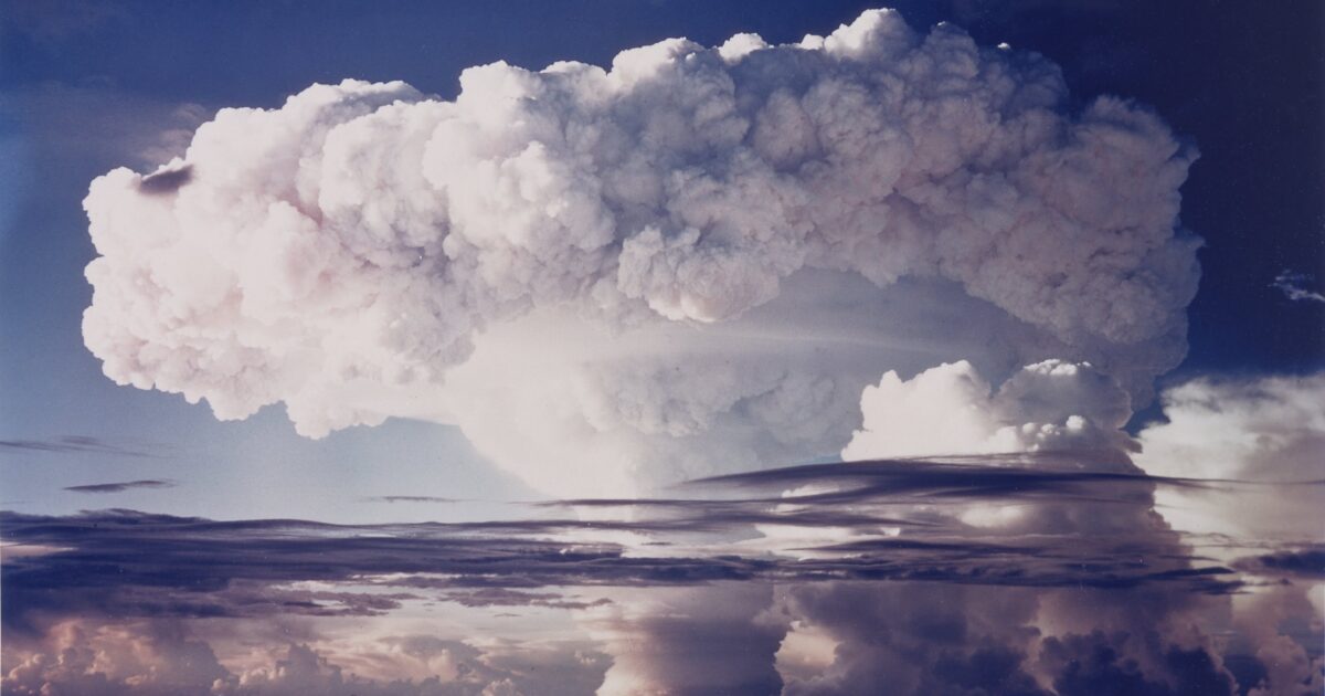 Mushroom cloud formation rising above the horizon, showcasing dramatic atmospheric effects and cloud textures against a blue sky.