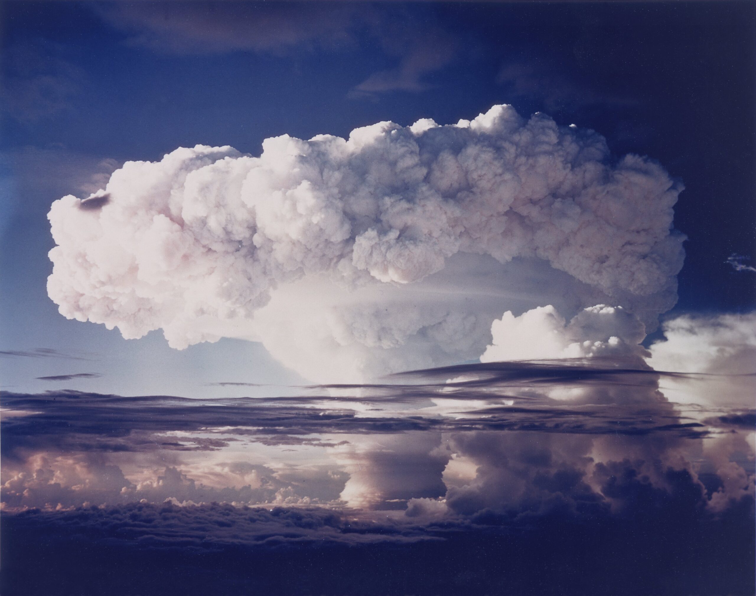 Mushroom cloud formation rising above the horizon, showcasing dramatic atmospheric effects and cloud textures against a blue sky.