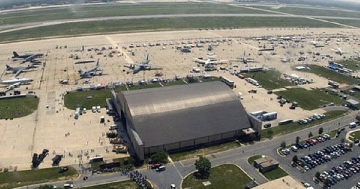 Aerial view of an airport showcasing various aircraft, hangars, and parking areas, highlighting aviation events or activities.
