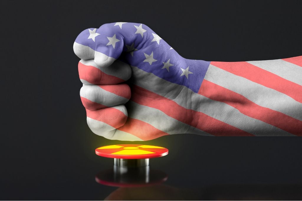 Fist covered in the American flag poised above a red button, symbolizing power and potential decision-making in a dramatic context.