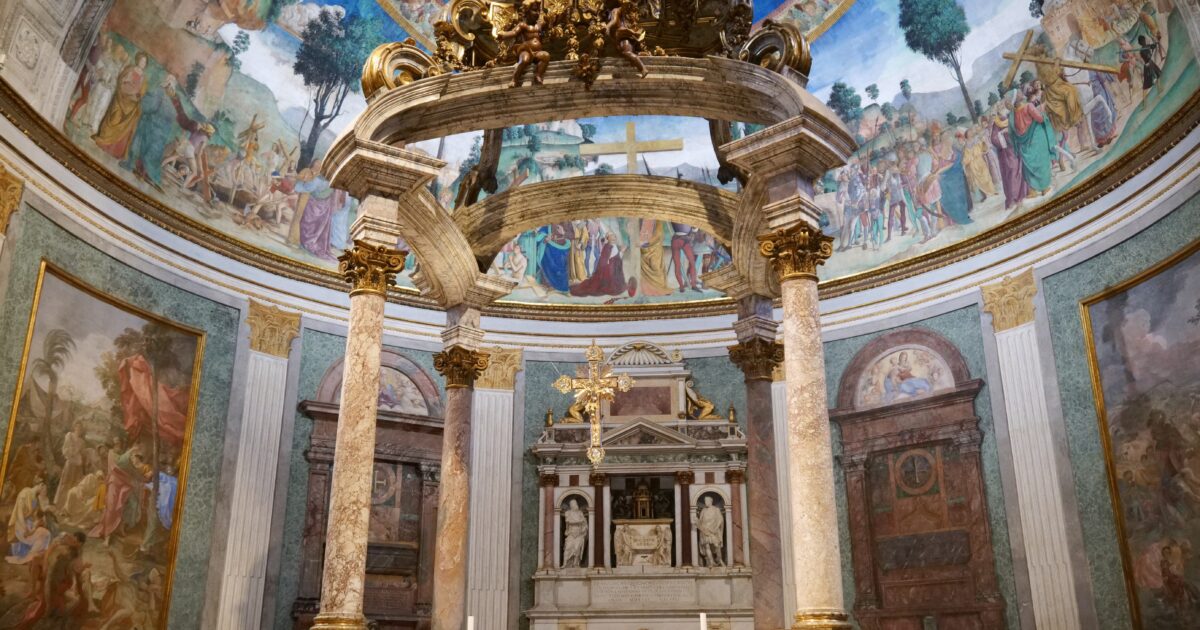 Interior view of a beautifully decorated church featuring intricate frescoes, ornate columns, and a central altar with a cross and sculptures.