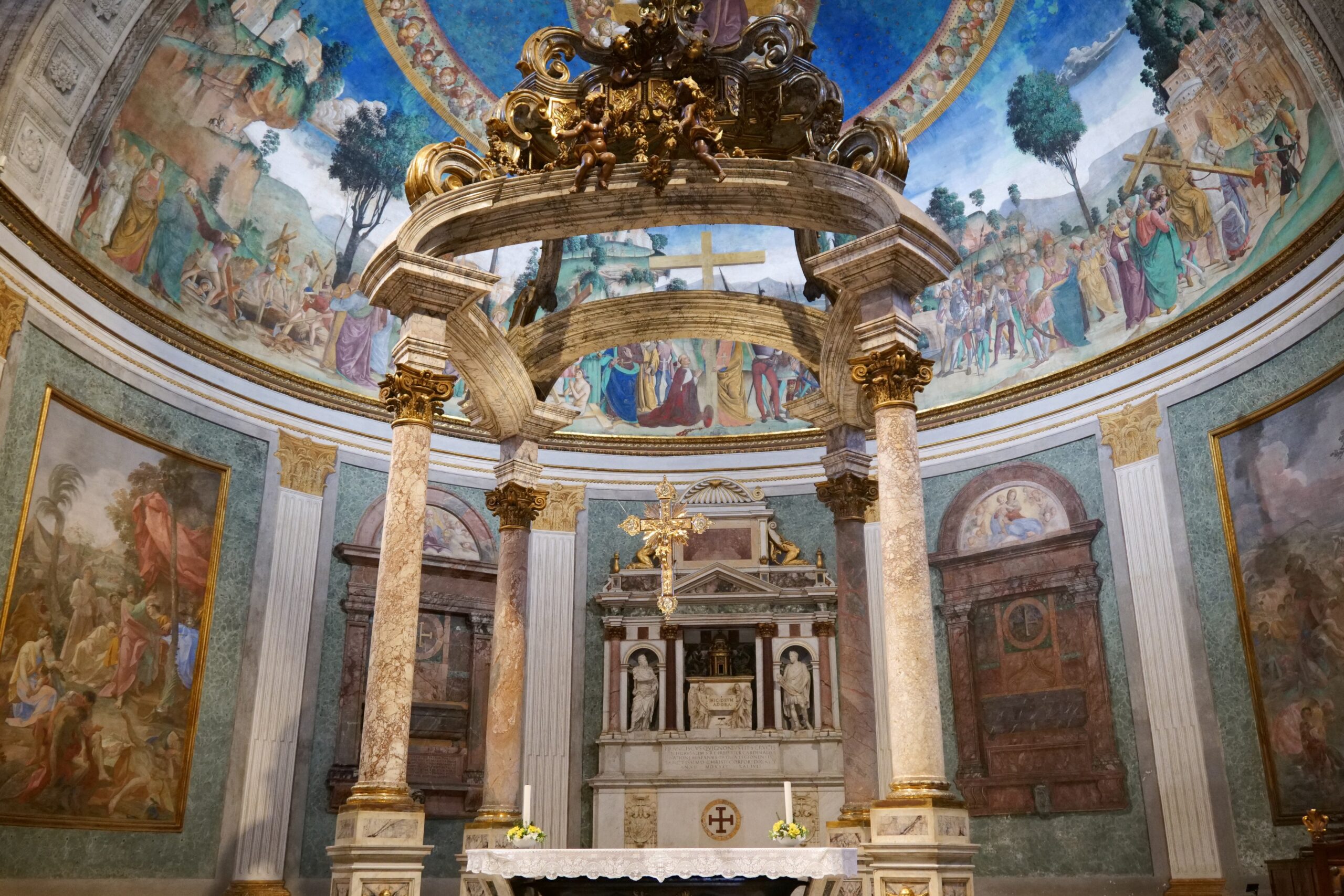 Interior view of a beautifully decorated church featuring intricate frescoes, ornate columns, and a central altar with a cross and sculptures.