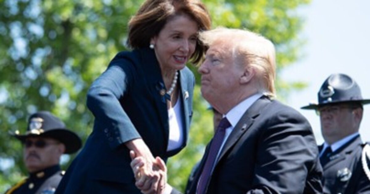Nancy Pelosi and Donald Trump engage in a handshake during a public event, with law enforcement officers visible in the background.