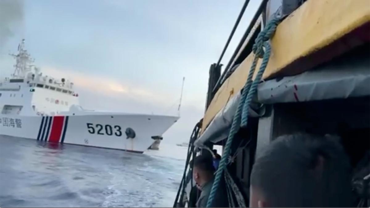 A close-up view of a fishing vessel alongside a large coast guard ship marked with the number 5203, set against a cloudy sky.