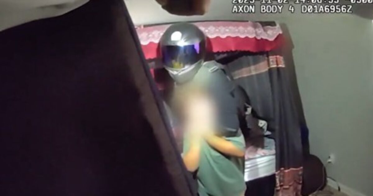 Body camera footage capturing a scene in a bedroom with two individuals, one wearing a motorcycle helmet, in a domestic setting.