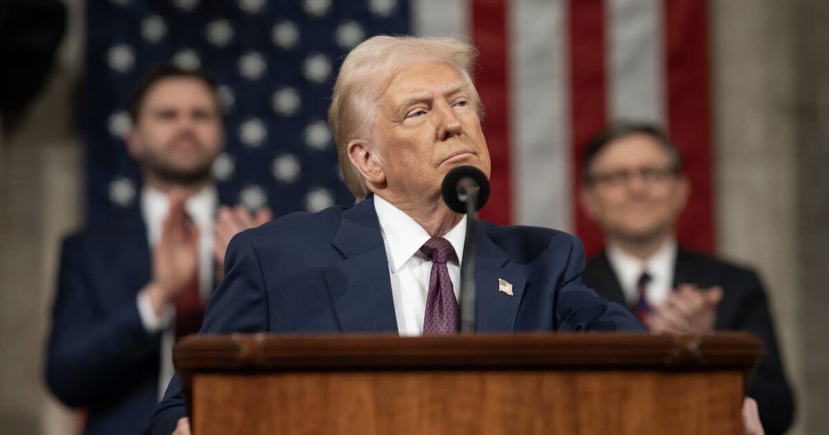Donald Trump delivers a speech at a podium with the American flag in the background, while supporters applaud in the audience.