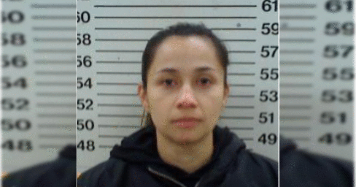 Mugshot of a woman against a height chart, wearing a black jacket, with a neutral expression and straight black hair.