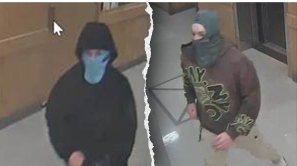 Two individuals wearing masks and hoodies captured on surveillance footage in a hallway, possibly involved in suspicious activity.