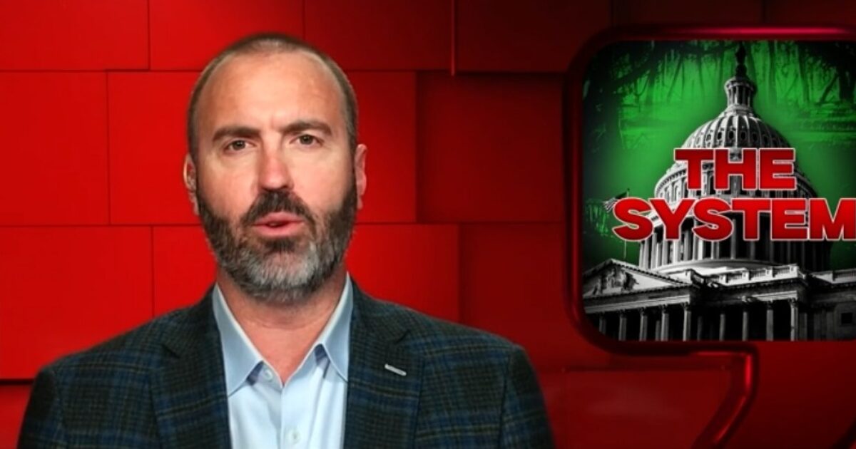 Presenter discussing political themes with a backdrop featuring the U.S. Capitol and the text "The System," highlighting issues related to governance and societal structures.