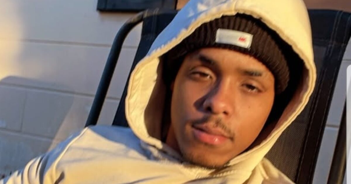 Young man wearing a beige hoodie and black beanie, sitting casually in a chair with sunlight illuminating his face.