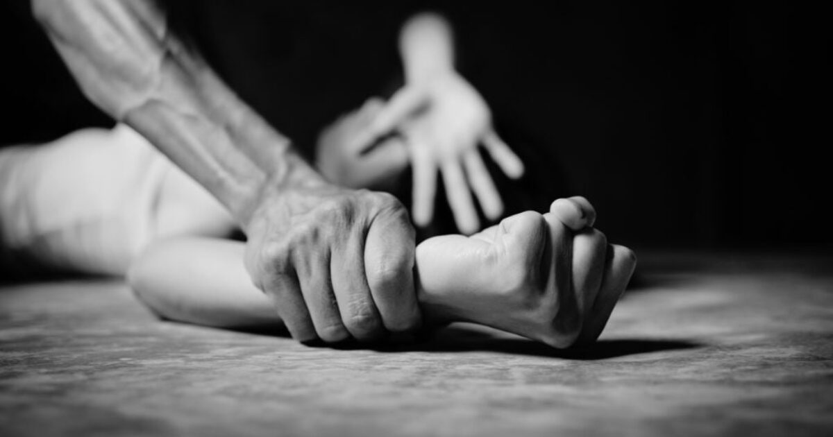 A close-up of a hand gripping another person's wrist, conveying a sense of struggle and tension in a dramatic black and white setting.