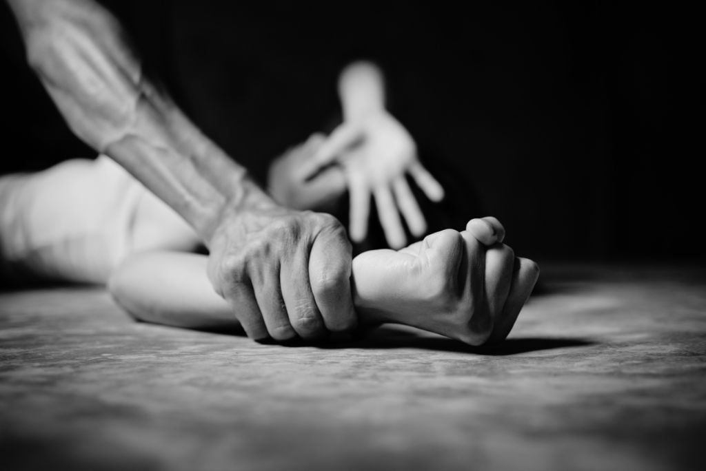 A close-up of a hand gripping another person's wrist, conveying a sense of struggle and tension in a dramatic black and white setting.