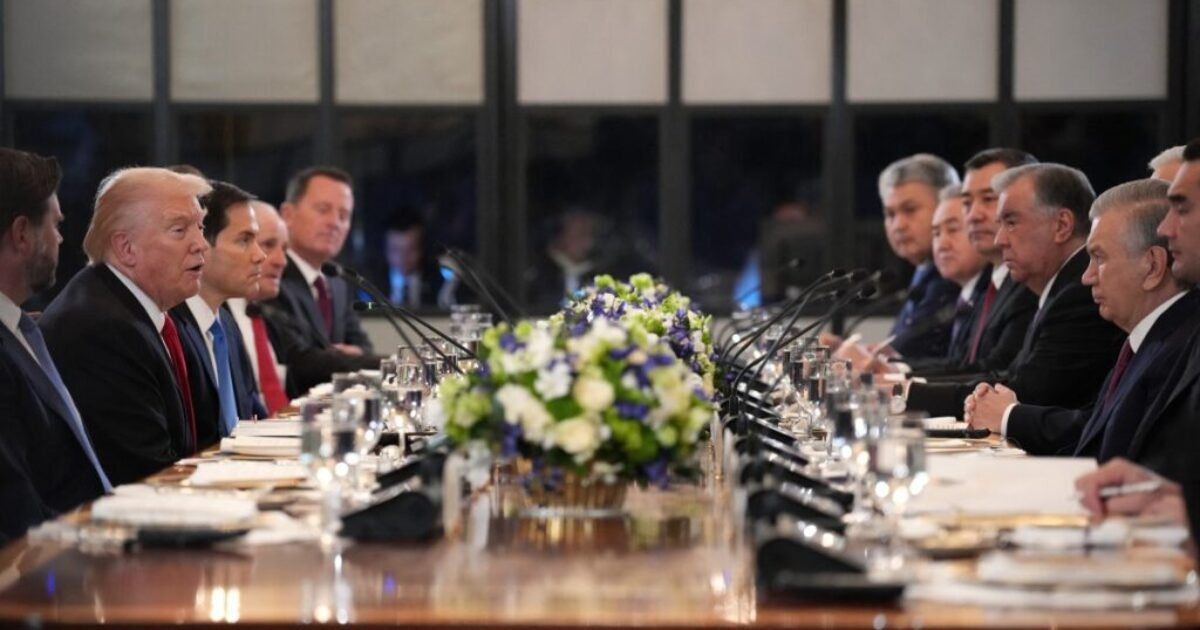 Leaders engaged in a formal discussion at a long table adorned with flowers, featuring Donald Trump and other officials during a diplomatic meeting.