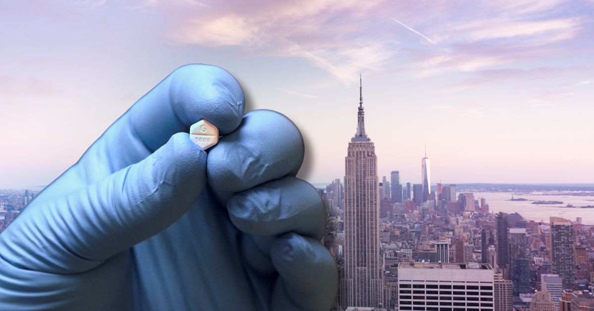 Gloved hand holding a medication tablet with the New York City skyline in the background, showcasing urban healthcare innovations.