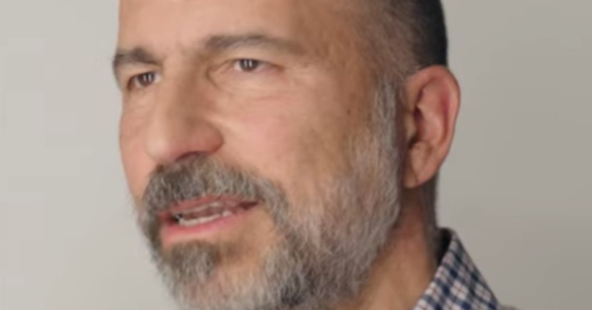 Close-up of a man with a beard speaking, wearing a checked shirt against a neutral background, conveying a thoughtful expression.