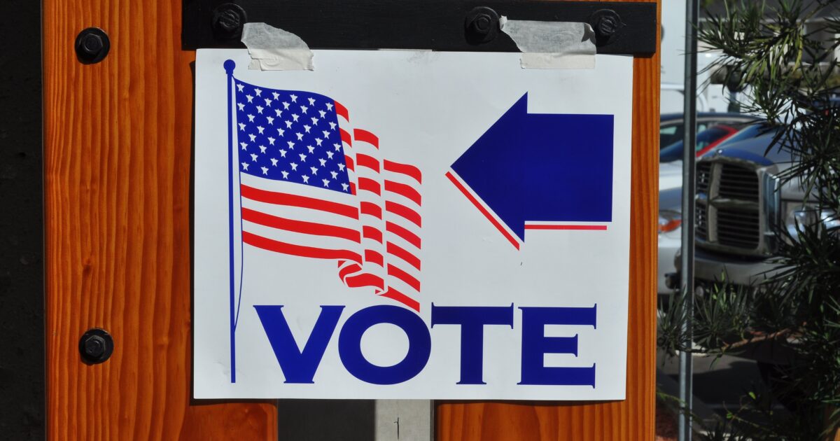 Voting sign with American flag and arrow directing voters to polling location.