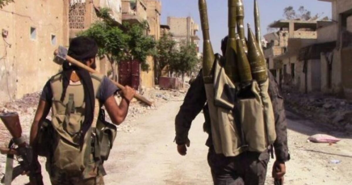 Two armed soldiers walk through a war-torn street, one carrying an axe and the other a backpack loaded with explosive projectiles.