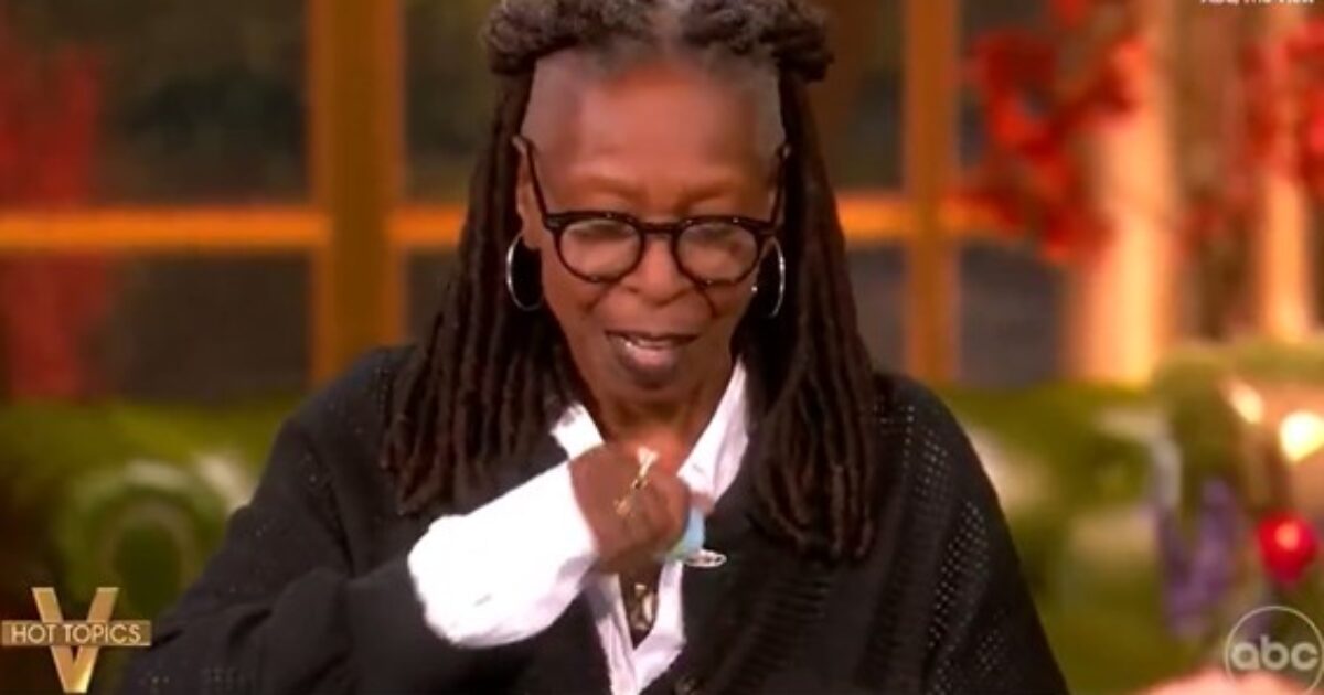 Whoopi Goldberg discussing a topic on "The View," wearing glasses and a black cardigan, with a thoughtful expression in a colorful studio setting.