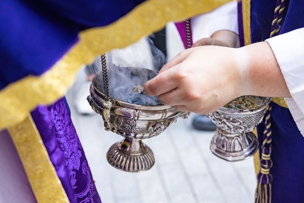 A close-up of a person holding a silver incense burner, releasing aromatic smoke during a ceremonial ritual.